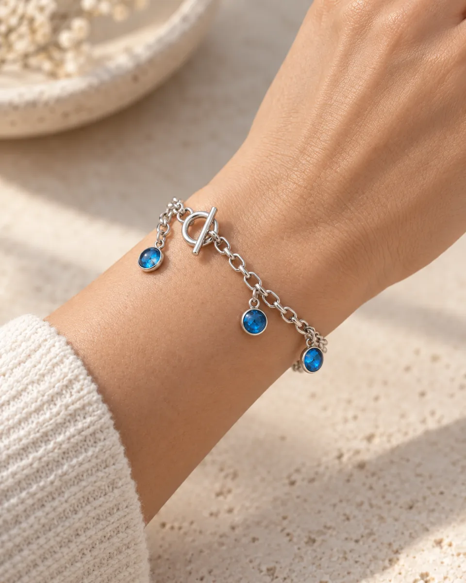 The same silver bracelet with three blue charms worn on a wrist