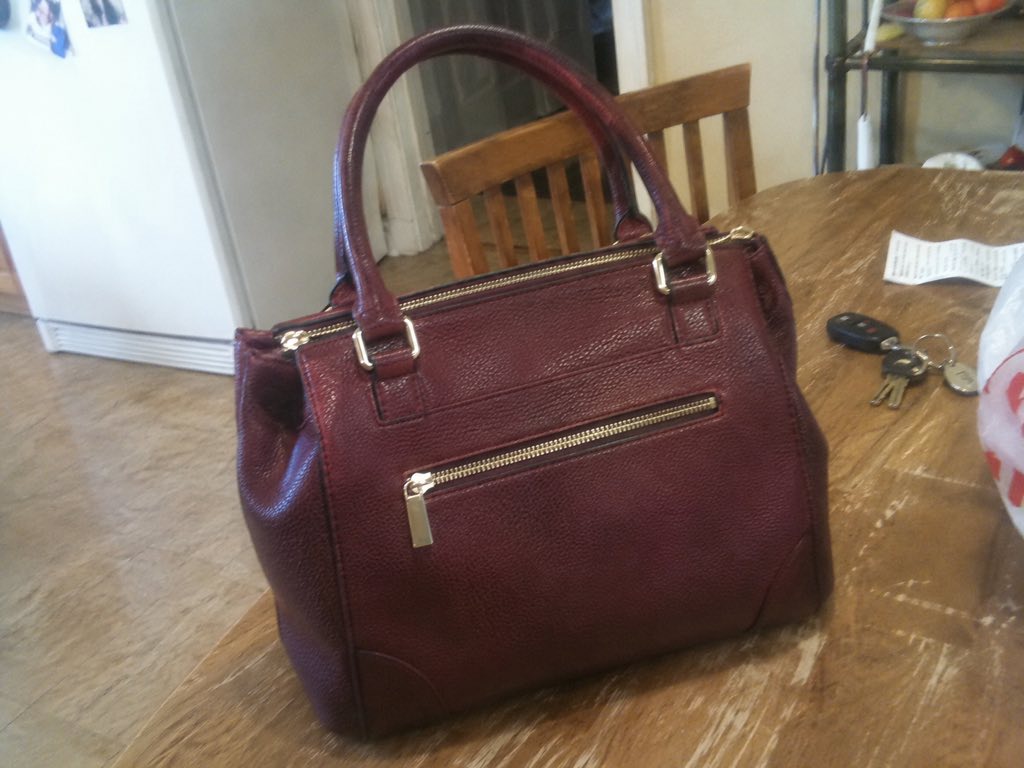 A burgundy handbag photographed on a cluttered kitchen table