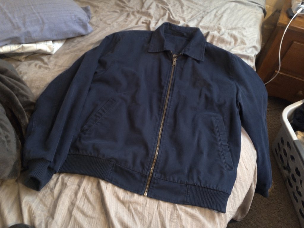 A dark navy jacket photographed on a bed in a cluttered room