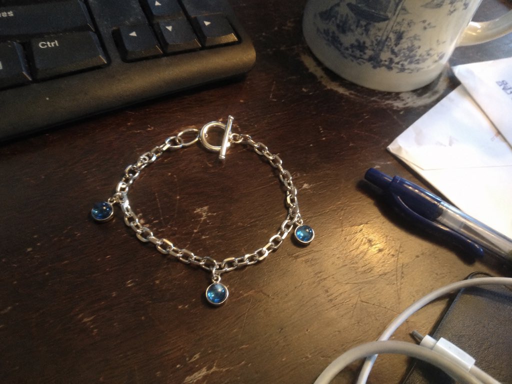 A silver bracelet with blue charms photographed on a cluttered desk